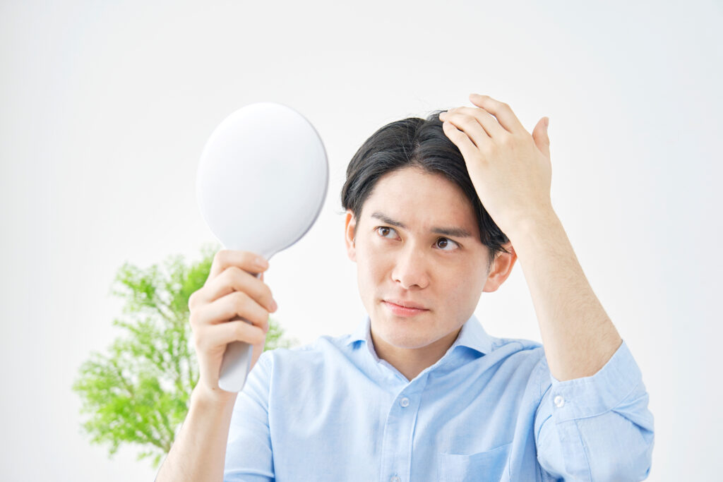 手鏡を持って髪の生え際を気にする水色のシャツを着た男性