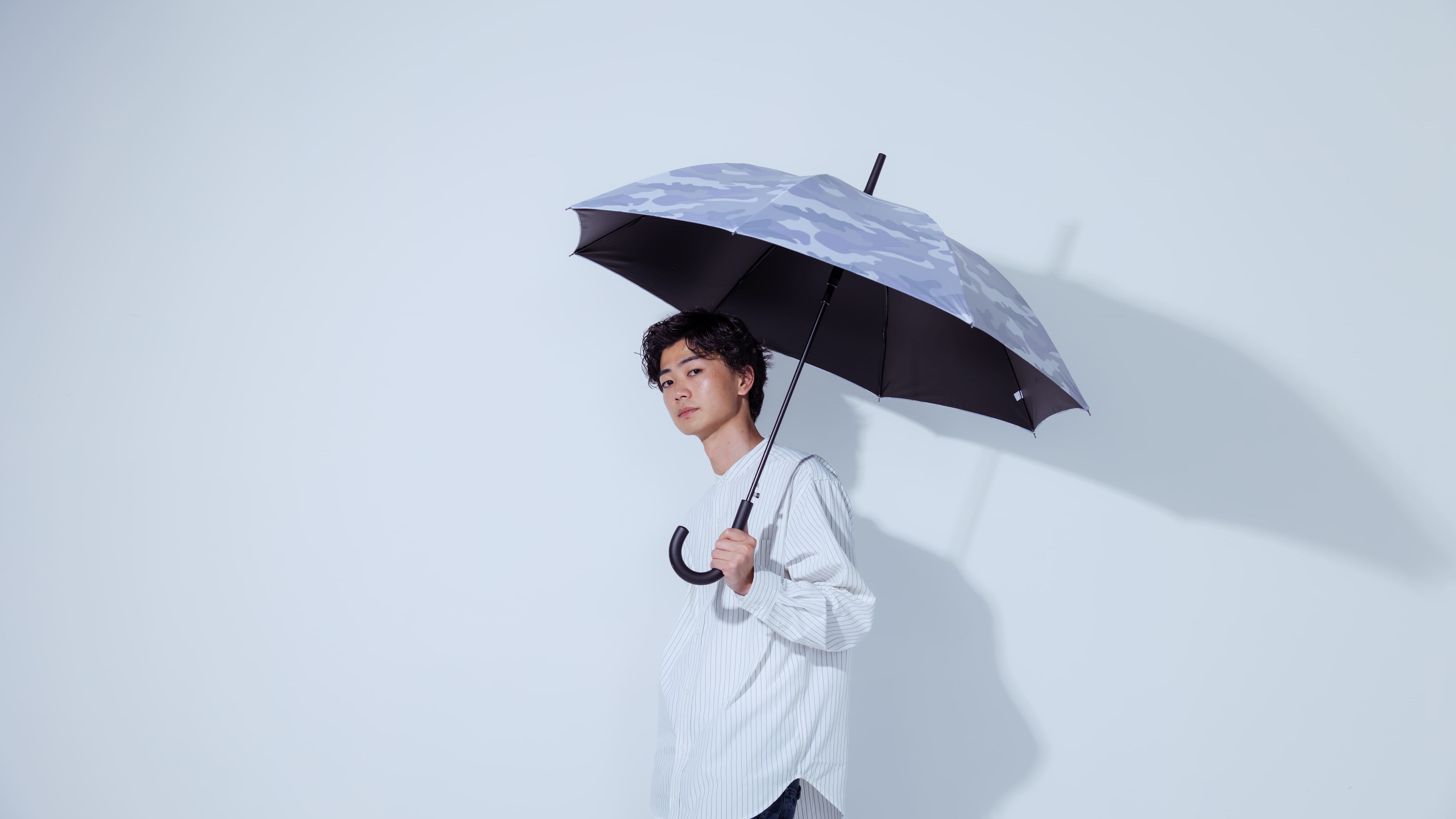 グレーの迷彩柄の傘を持ってこちらを向く男性