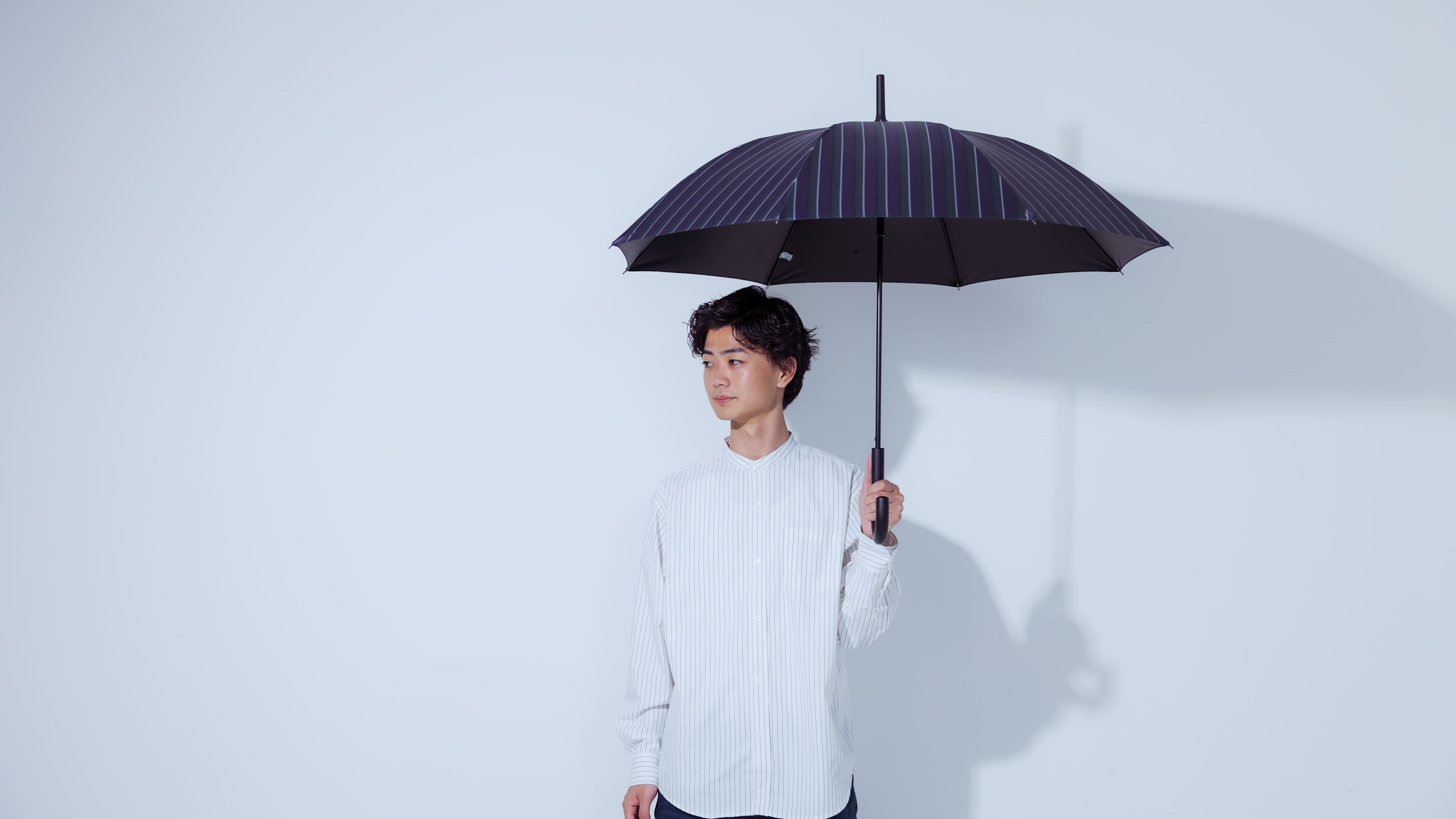 黒のストライプ柄の傘を持って横を向く男性