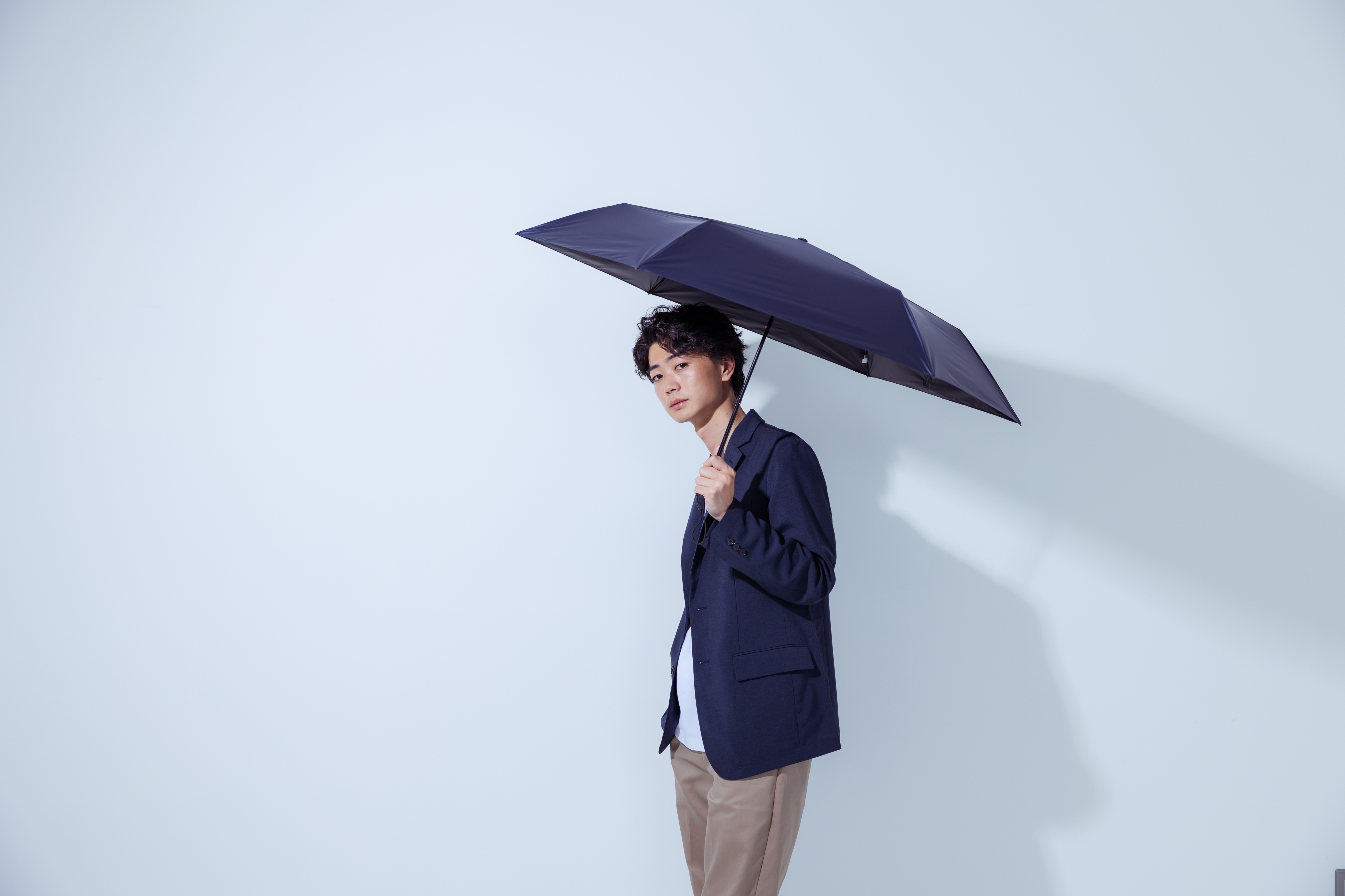白い背景をバックに日傘を持ってこちらを見ている男性