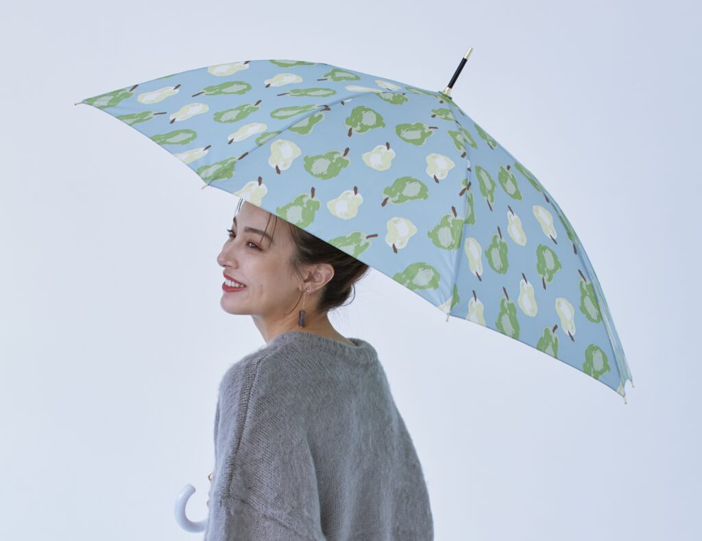 ラ・フランス柄の傘を持ってほほ笑む女性